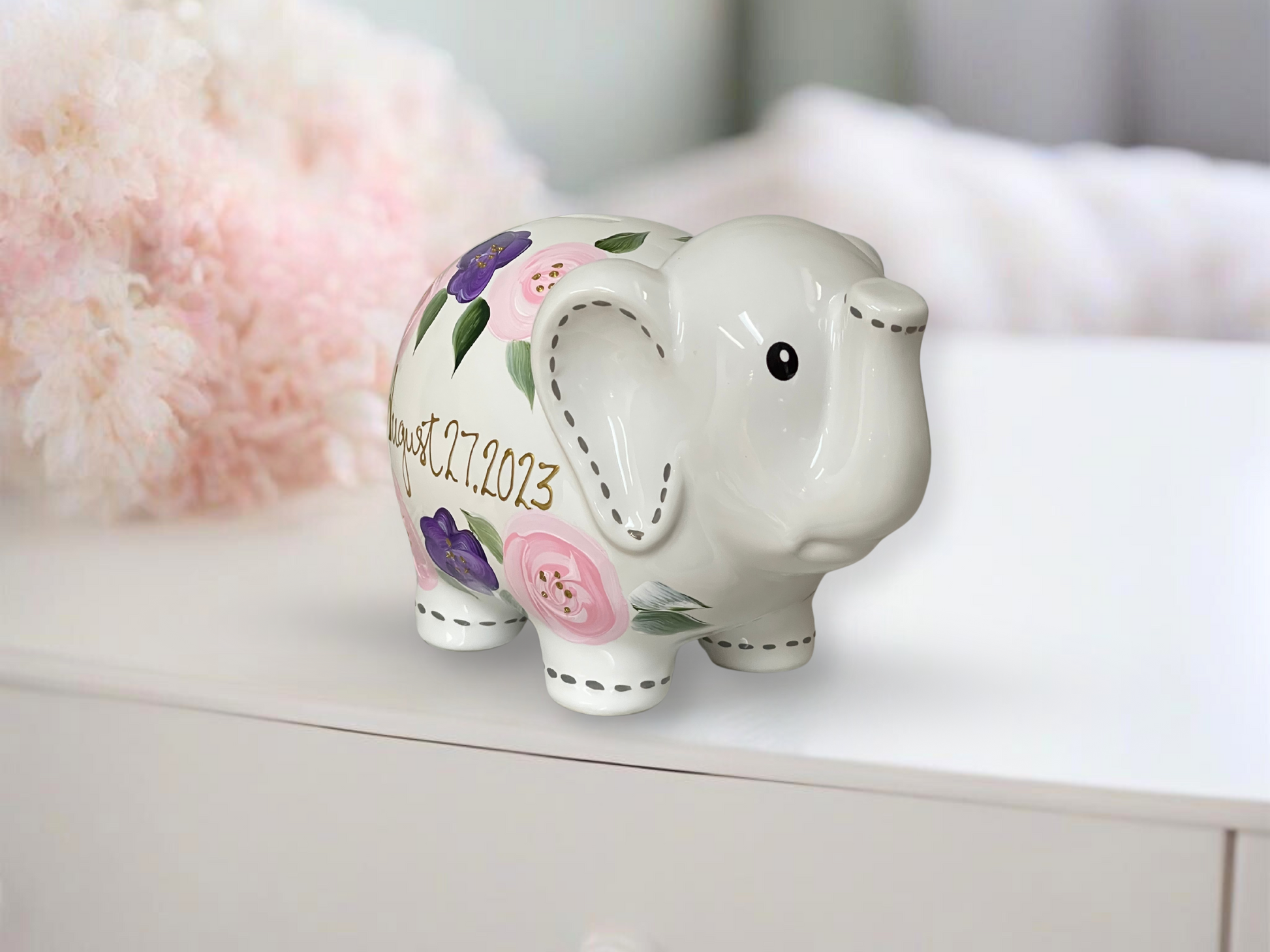 Hand-painted piggy bank adorned with delicate purple and pink flowers, offering a charming and personalized touch.