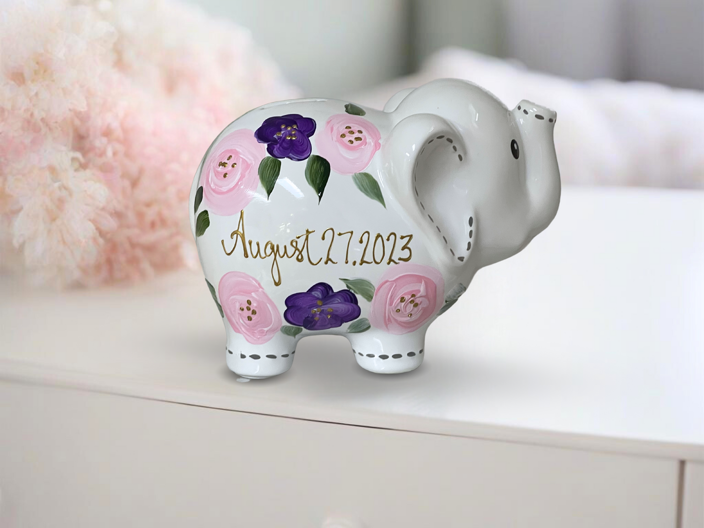 Hand-painted piggy bank adorned with delicate purple and pink flowers, offering a charming and personalized touch.