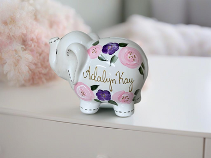 Hand-painted piggy bank adorned with delicate purple and pink flowers, offering a charming and personalized touch.